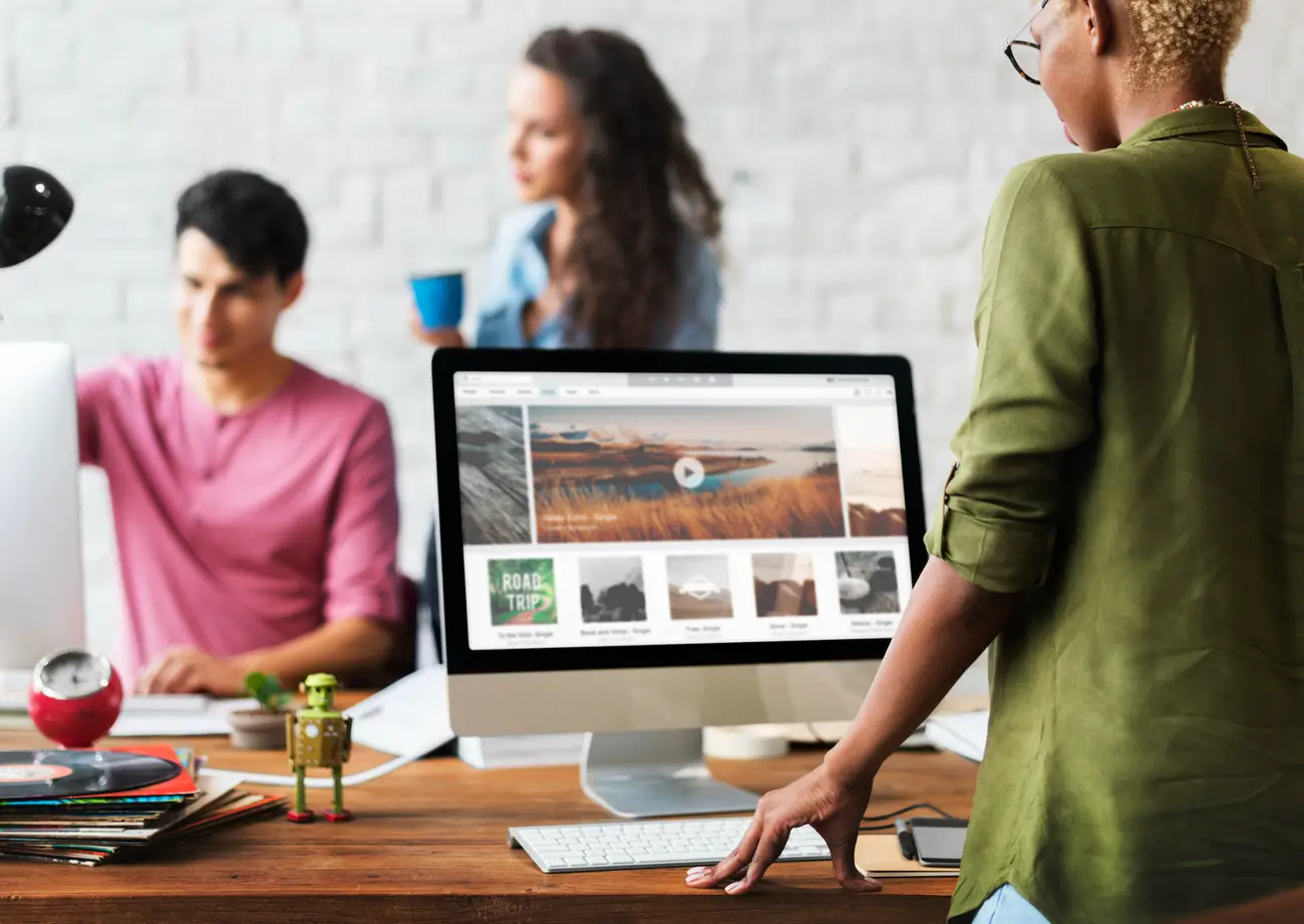 Person uses a computer with while two colleagues talk in the background of a modern office.