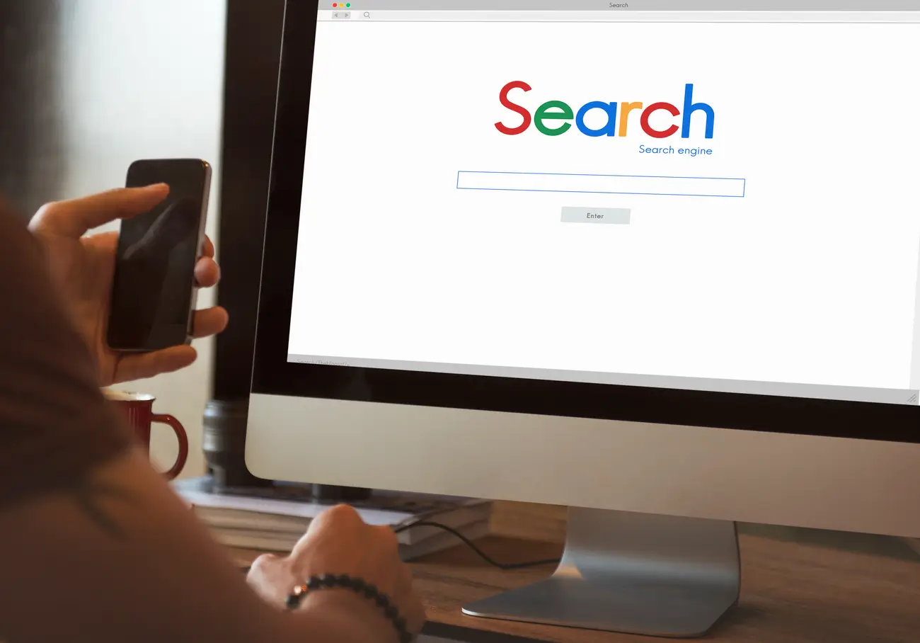Search engine homepage on computer with person holding smartphone