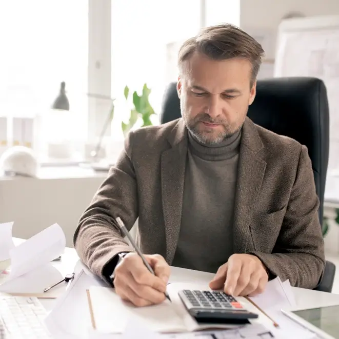 Man in a suit working at a desk with paperwork.