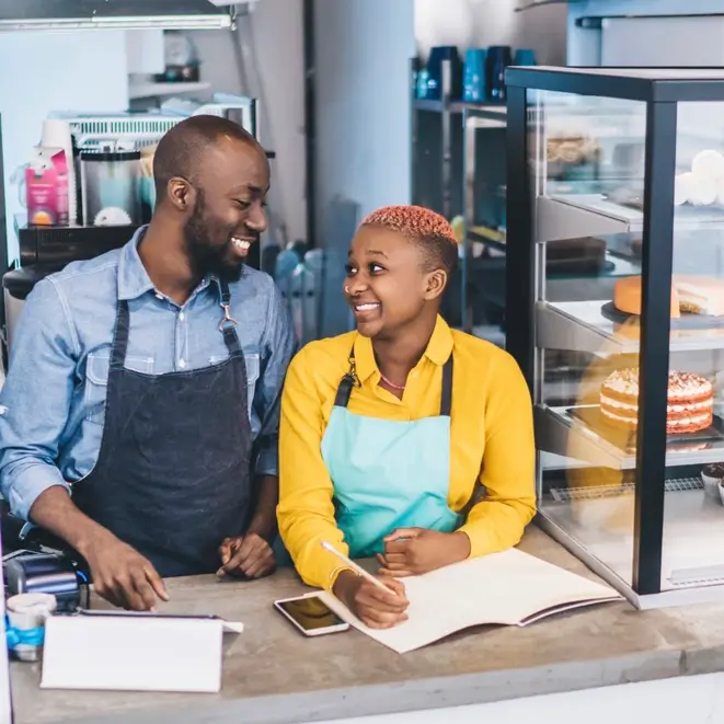 Two bakery staff smiling behind the counter.