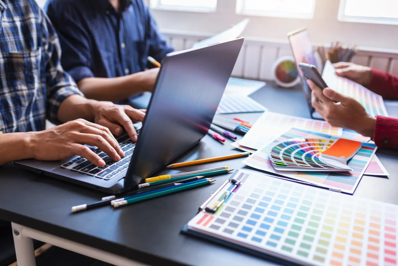 Three people collaborating on a design project with a laptop and colour samples